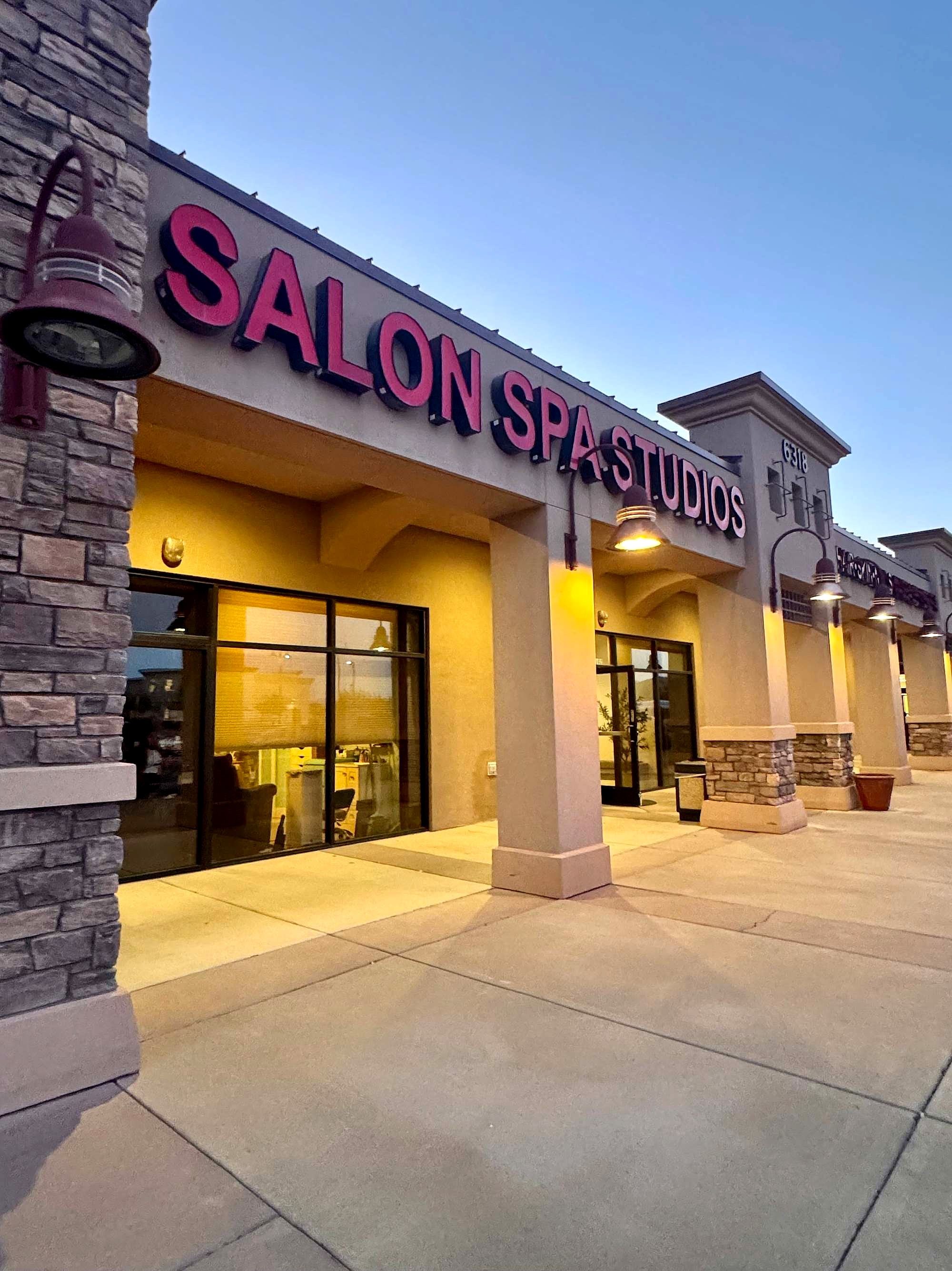 Salon Spa Studios at dusk, its sign lit pink, on South Higley Road