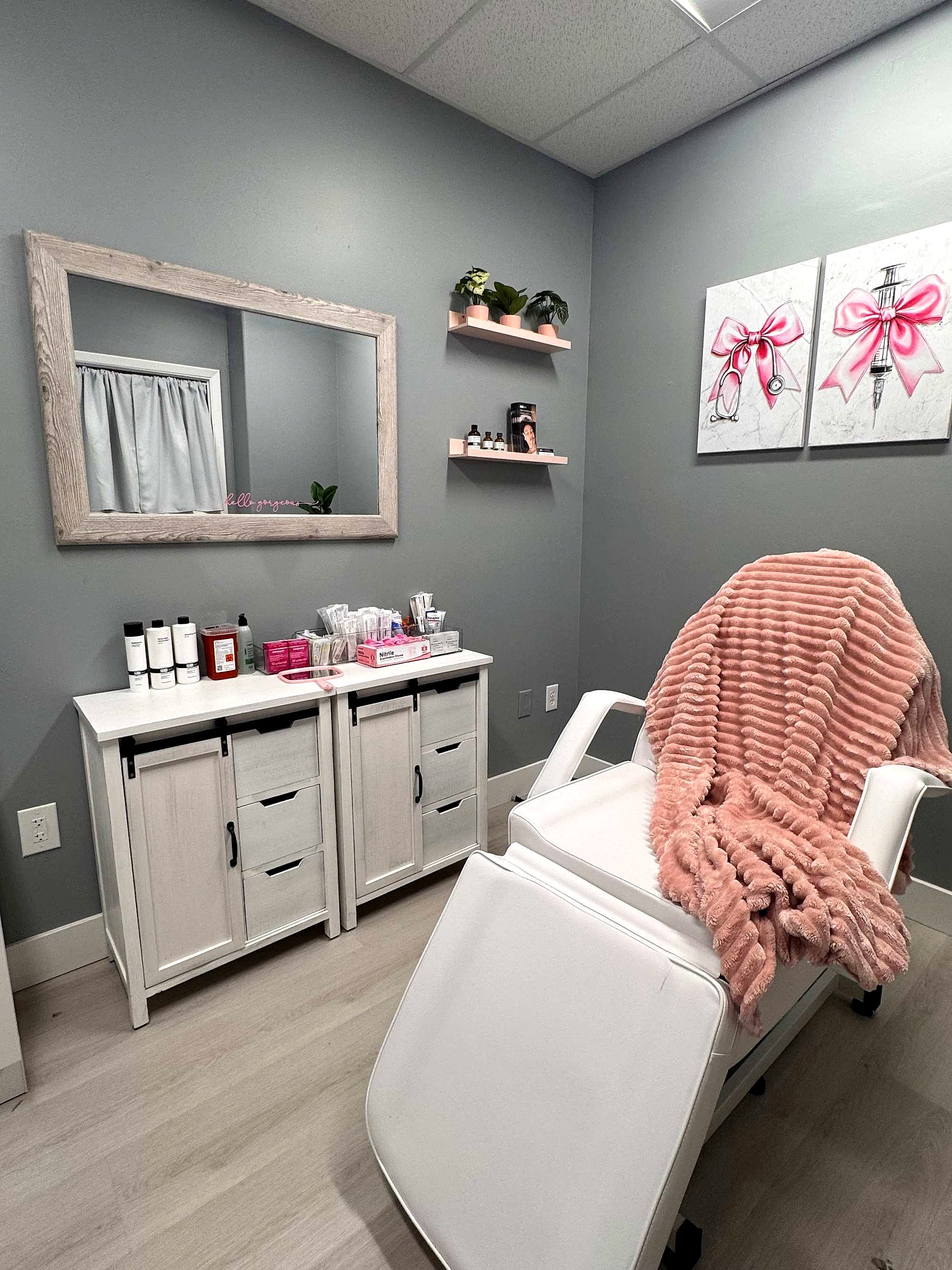 Kristine’s treatment room: white chair with a blush throw, mirror and pink bow canvases on grey walls